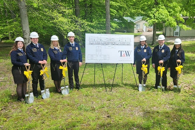 Indiana FFA members stand beside an architectural diagram of the new ADA-compliant cabin with ceremonial groundbreaking shovels.