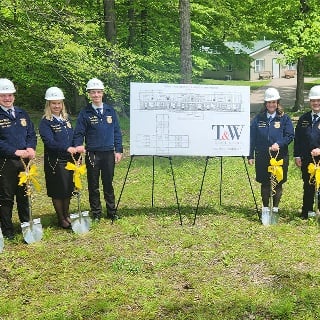 Indiana FFA members stand beside an architectural diagram of the new ADA-compliant cabin with ceremonial groundbreaking shovels.