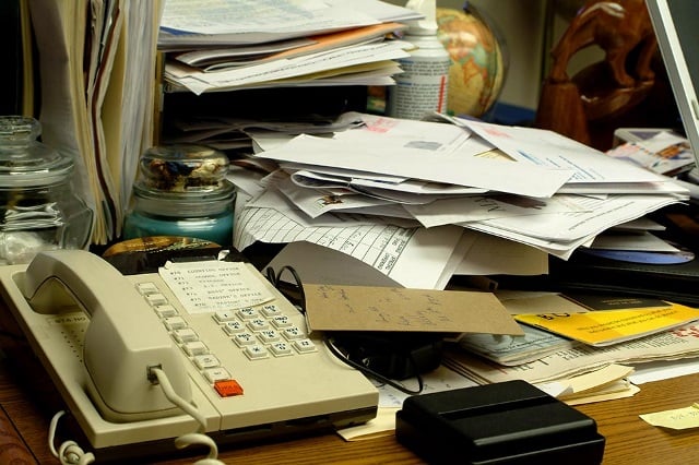 An office desk littered with papers and a landline phone