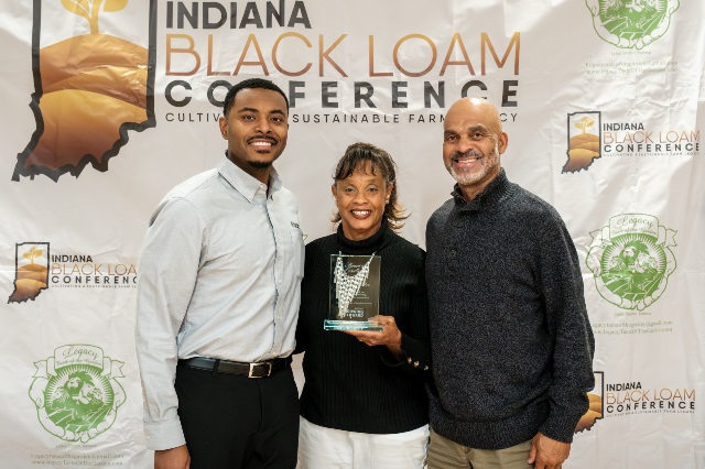 Two men stand on either side of a woman holding Farm Credit Mid-America's Community Excellence Award.