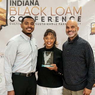 Two men stand on either side of a woman holding Farm Credit Mid-America's Community Excellence Award.