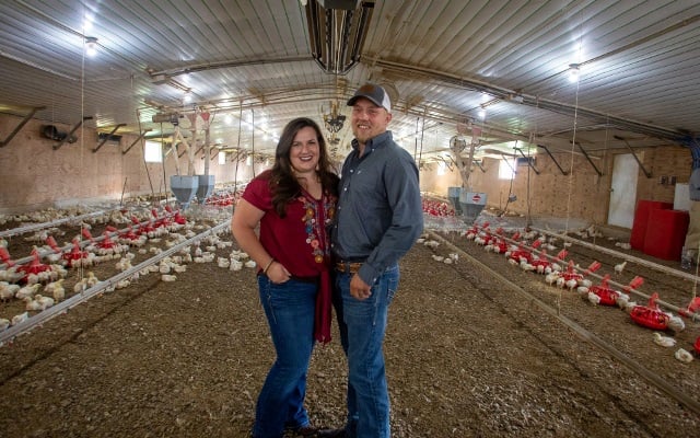 Man and woman stand in the middle of a broiler house.