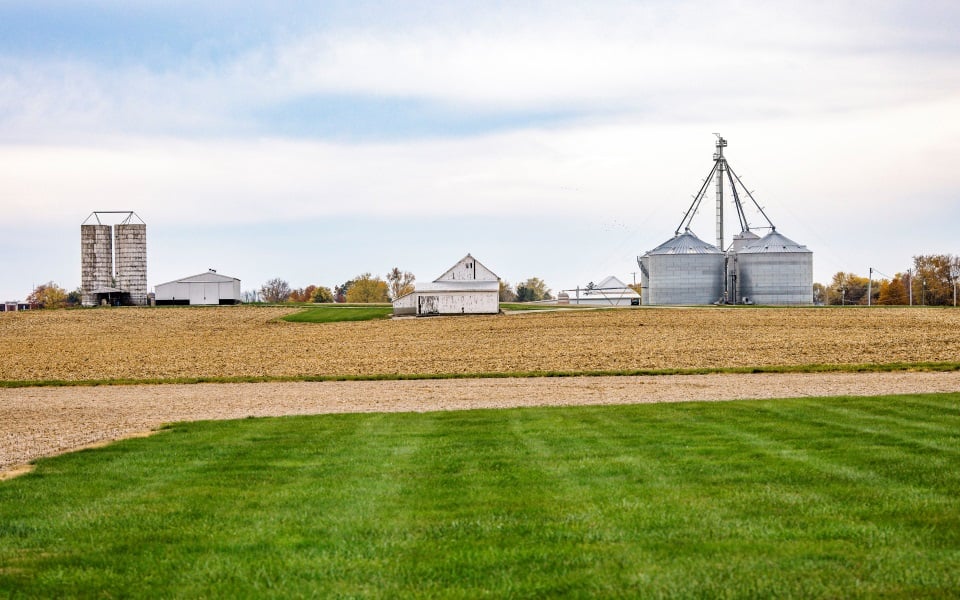 Farm landscape with white barn and metal grain bins.