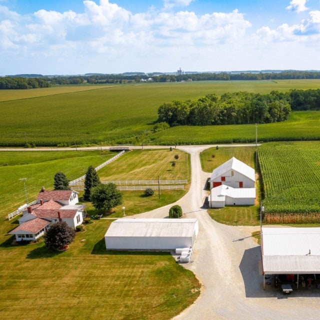 Aerial farm landscape with white barn and green corn fields.