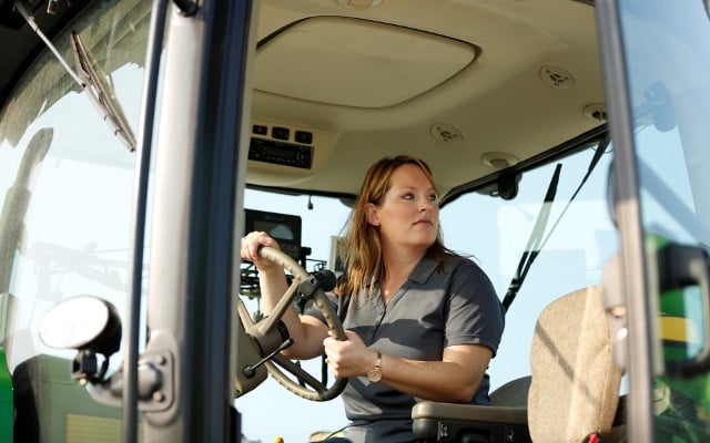 Woman in the cab of a tractor.