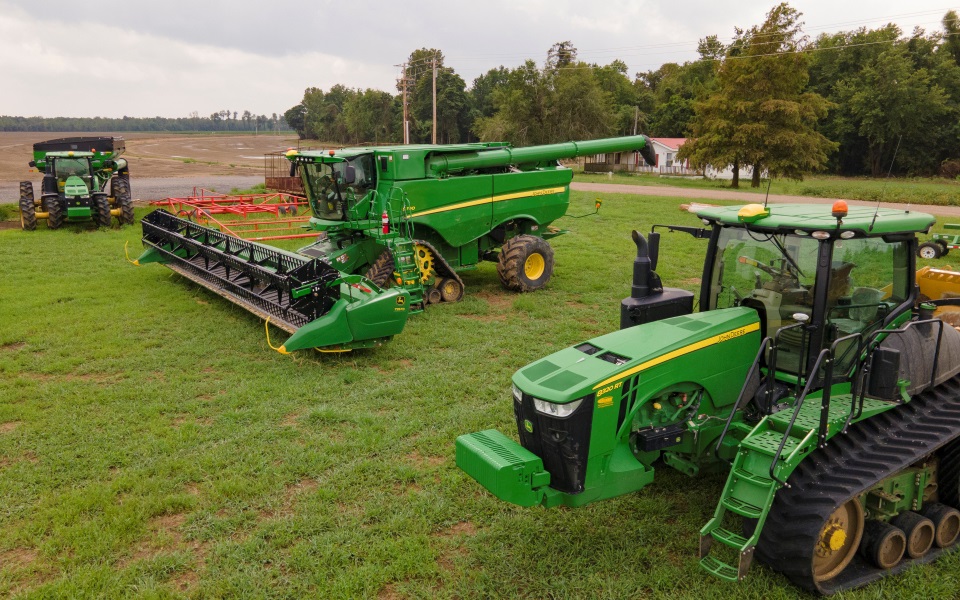 Green tractor and green combine with soybean head.