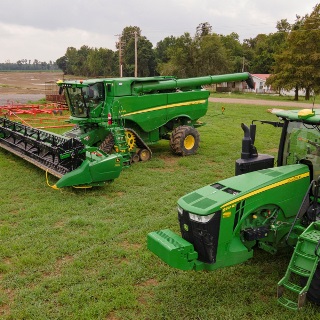 Green tractor and green combine with soybean head.