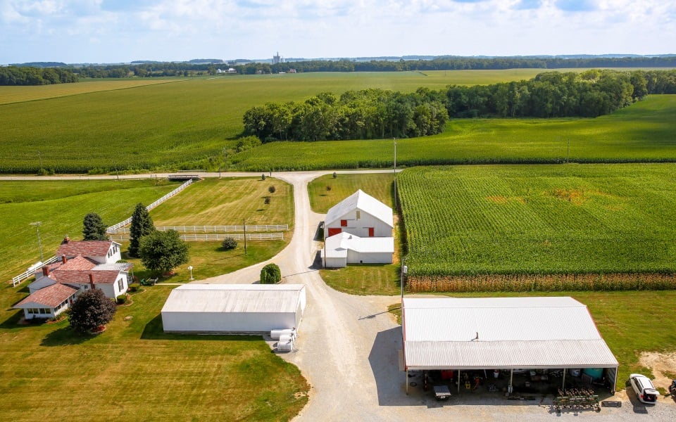 Aerial farm landscape with white barn and green corn fields.