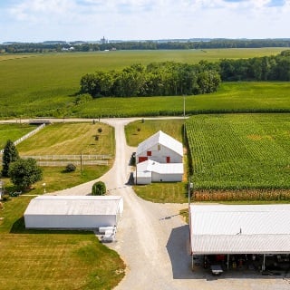 Aerial farm landscape with white barn and green corn fields.