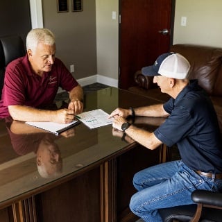 Two men sit at an office desk looking at documents.