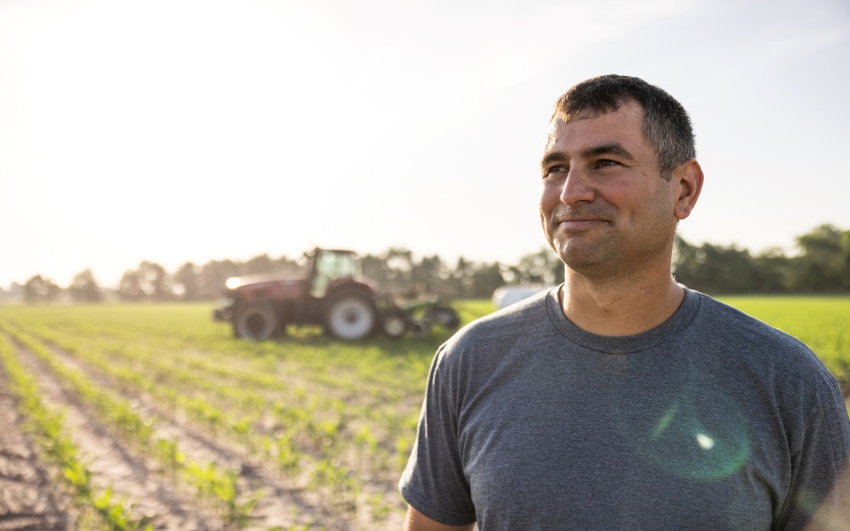 Young farmer stands in a recently planted corn field