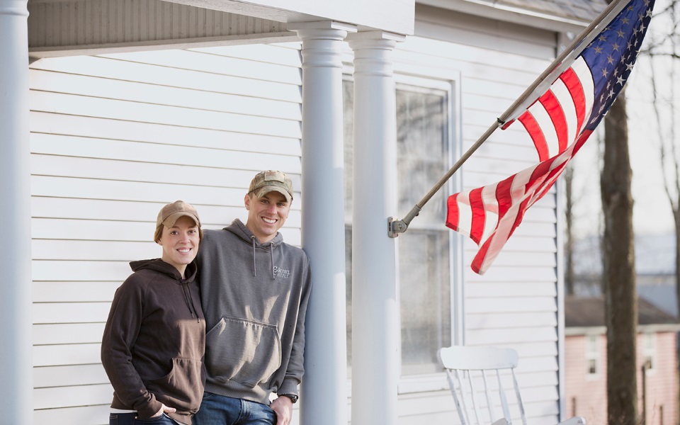 Woman and man stand next to American flag.