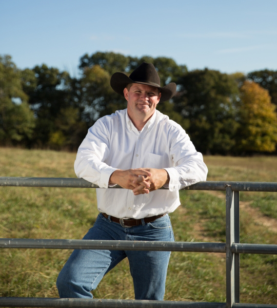 Man leans on gate in front of field.