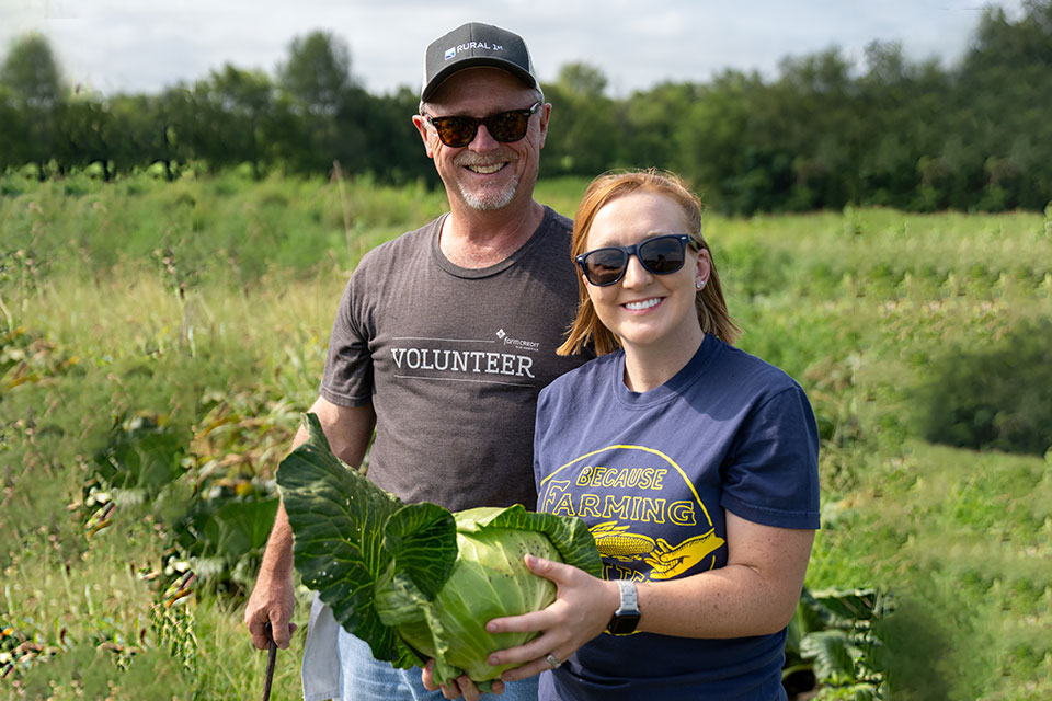 A man and woman hold a large head of cabbage in a field.