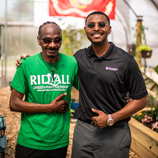 A man with a Rid-All Green Partnership t-shirt poses with a man in a Farm Credit Mid-America polo shirt.
