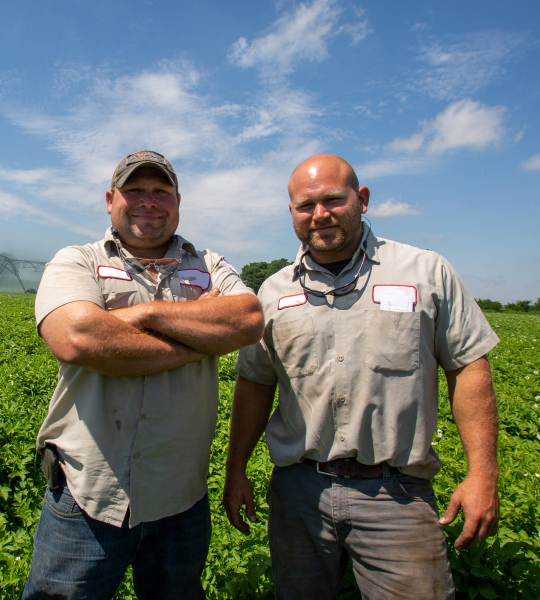 Two men stand in a green field.