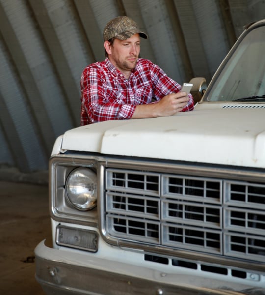 Man checks his phone on the hood of an old white truck.