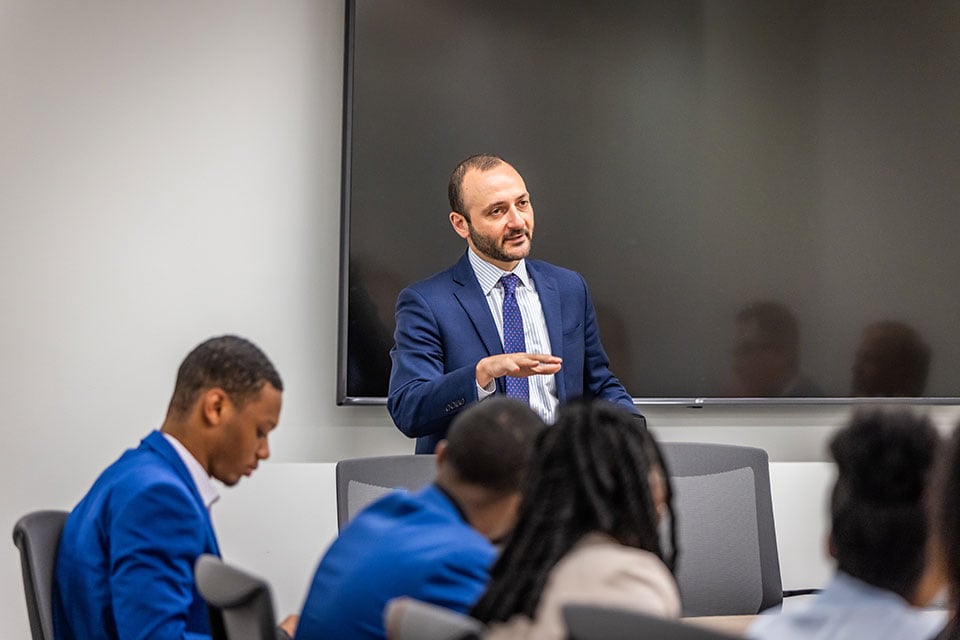 A man in a suit talks to a Farm Credit Mid-America Scholars cohort in a conference room.