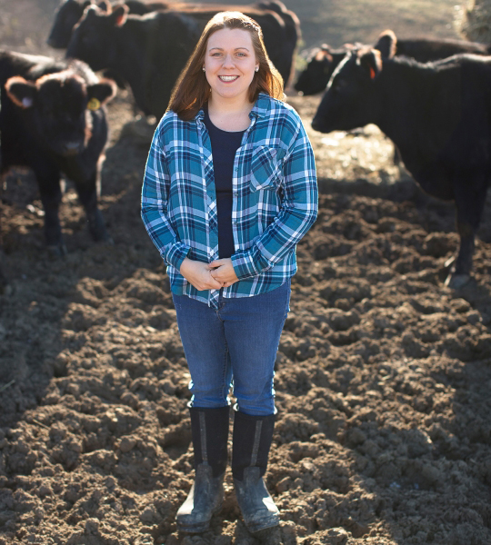 High school girl stands in cattle field.