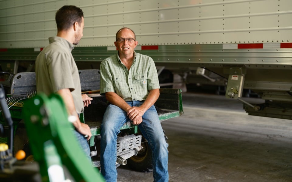 Farmer sits on back of UTV talking to loan officer about his farm's balance sheet