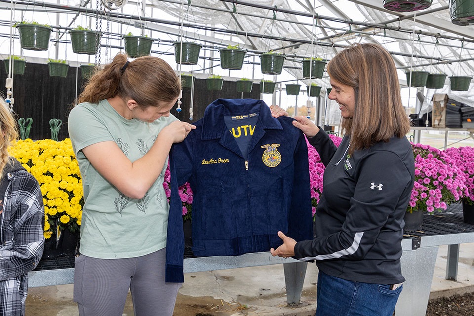 Two women hold up a FFA jacket with one of their names embroidered on it.