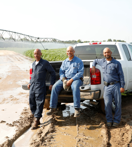 Three men sit on a truck tailgate.