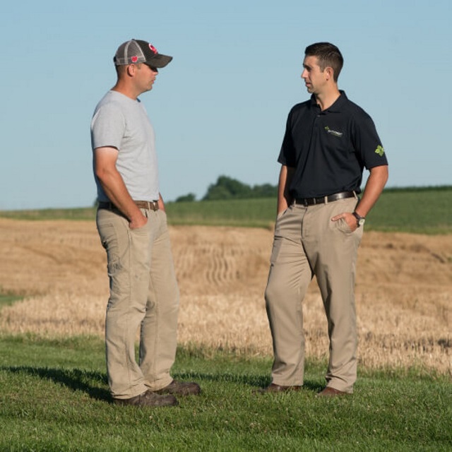 Two men talk in front of a harvested field.