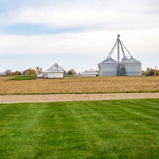 Farm landscape with white barn and grain bins.