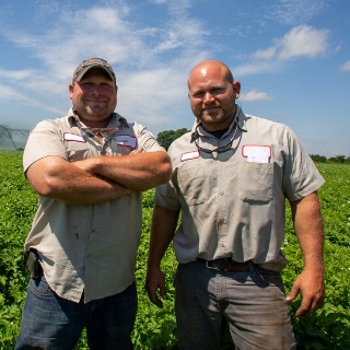 Two men stand in a green field.