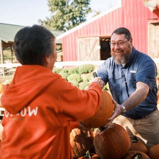 Man hands a pumpkin to a person in an orange hoodie.