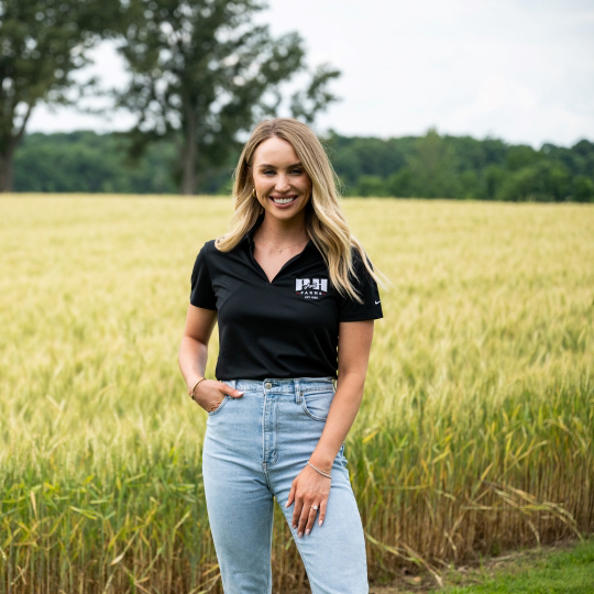 Young female farmer stands in front of wheat field